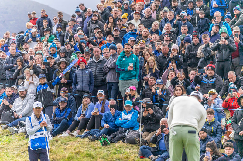 Rory McIlroy putts on the 9th green at Royal County Down watched by caddie Harry Diamond and fans during the 2024 Amgen Irish Open.
